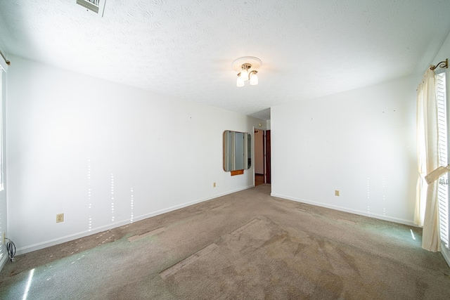 carpeted empty room with a textured ceiling, visible vents, and baseboards