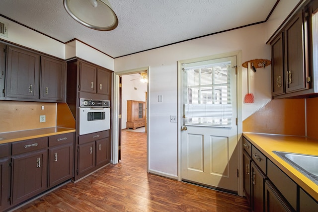 kitchen featuring dark brown cabinetry, dark wood-type flooring, white oven, a textured ceiling, and a sink