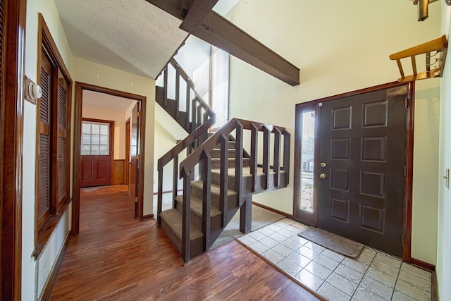 entrance foyer with a textured ceiling, wood finished floors, baseboards, stairs, and beam ceiling