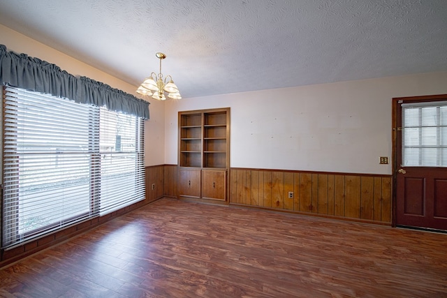 empty room with a chandelier, wainscoting, a textured ceiling, and wood finished floors