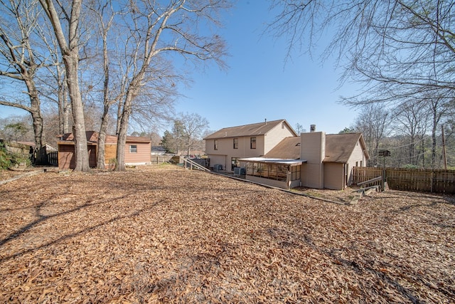 rear view of property featuring a chimney, fence, and an outdoor structure