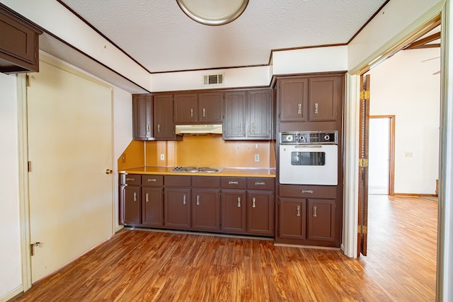 kitchen with stainless steel gas cooktop, a textured ceiling, wood finished floors, oven, and under cabinet range hood