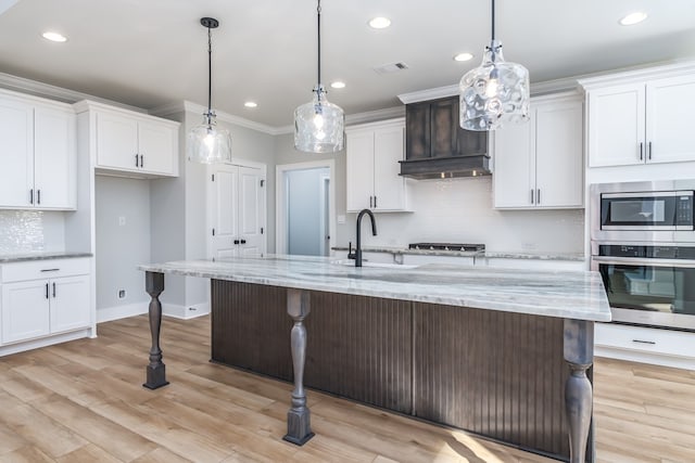 kitchen with an island with sink, white cabinets, stainless steel appliances, and decorative light fixtures