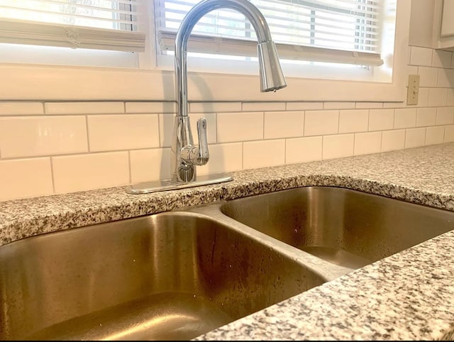 details with backsplash, light stone counters, and sink