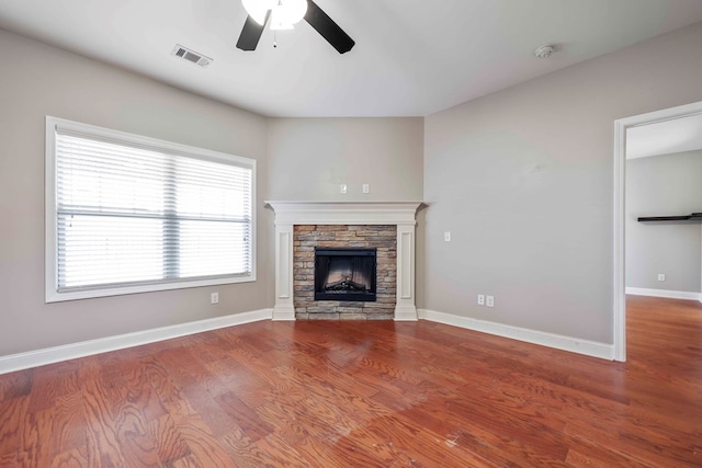 unfurnished living room featuring wood-type flooring, a stone fireplace, and ceiling fan