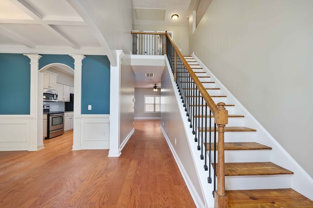 stairway with decorative columns, coffered ceiling, ceiling fan, beamed ceiling, and hardwood / wood-style floors