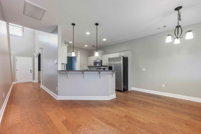 kitchen with stainless steel appliances, kitchen peninsula, pendant lighting, white cabinets, and light wood-type flooring