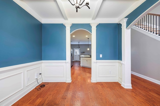 empty room with ornate columns, an inviting chandelier, beamed ceiling, and light wood-type flooring