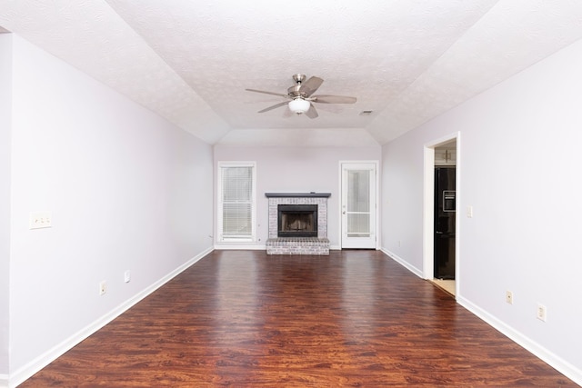 unfurnished living room with ceiling fan, dark wood-type flooring, a textured ceiling, and a brick fireplace