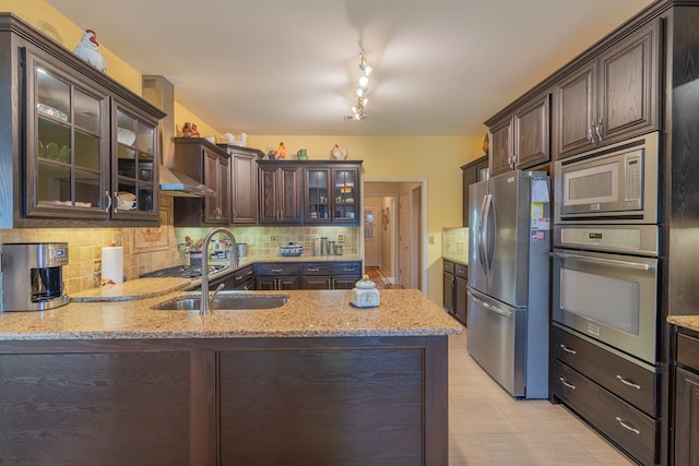 kitchen featuring light stone counters, tasteful backsplash, appliances with stainless steel finishes, glass insert cabinets, and dark brown cabinetry