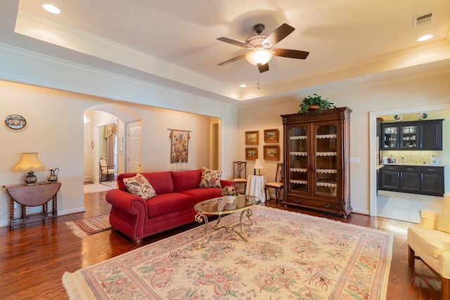 living area with visible vents, arched walkways, wood finished floors, and a raised ceiling