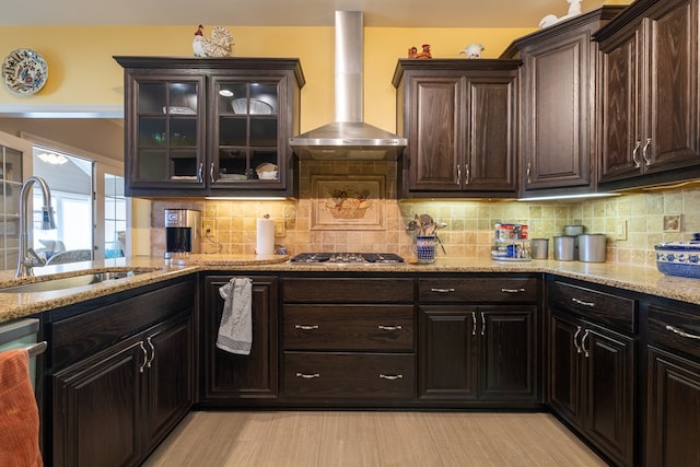 kitchen featuring a sink, wall chimney range hood, light stone countertops, dishwasher, and stainless steel gas stovetop