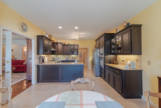 kitchen featuring glass insert cabinets, a peninsula, stainless steel appliances, dark brown cabinets, and a sink