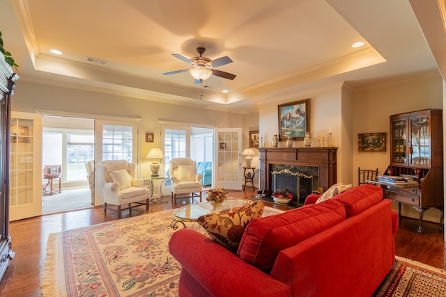 living room featuring a fireplace, visible vents, a raised ceiling, and wood finished floors