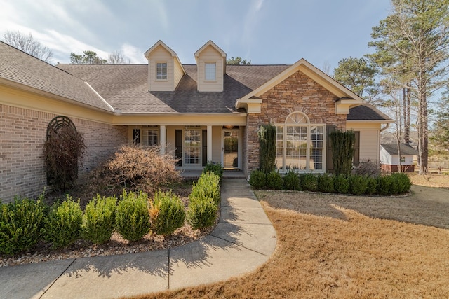 view of front of property with stone siding, a shingled roof, a porch, and brick siding