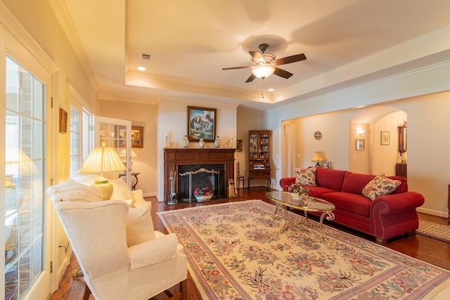 living area with a tray ceiling, crown molding, arched walkways, and wood finished floors