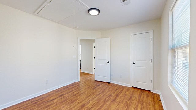 unfurnished bedroom with visible vents, baseboards, attic access, and light wood finished floors