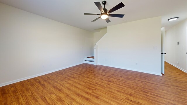 unfurnished living room with stairway, baseboards, light wood-style floors, and a ceiling fan