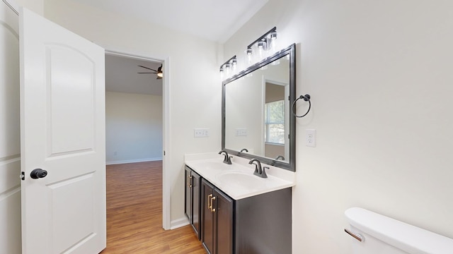 bathroom featuring ceiling fan, toilet, double vanity, wood finished floors, and a sink