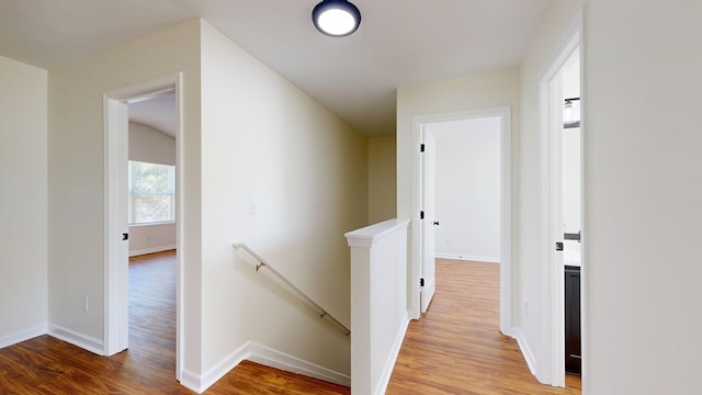 hall featuring light wood-type flooring, an upstairs landing, and baseboards