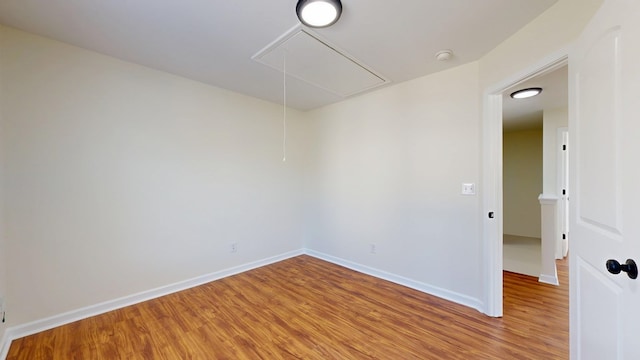 unfurnished room featuring baseboards, attic access, and light wood-style floors