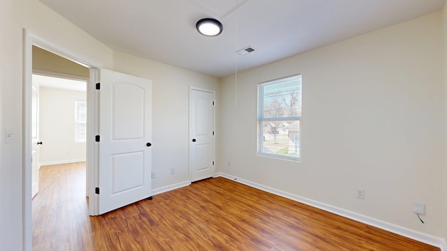 unfurnished bedroom with attic access, wood finished floors, baseboards, and visible vents