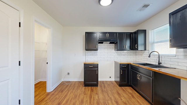 kitchen featuring visible vents, light wood-style flooring, a sink, backsplash, and baseboards