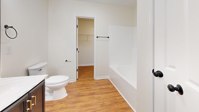 full bathroom with toilet, a washtub, wood finished floors, baseboards, and vanity