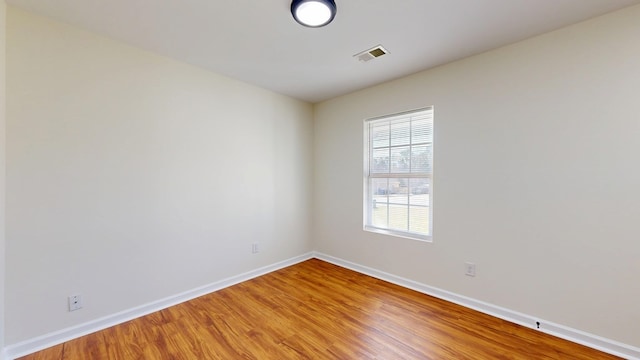 unfurnished room with light wood finished floors, visible vents, and baseboards