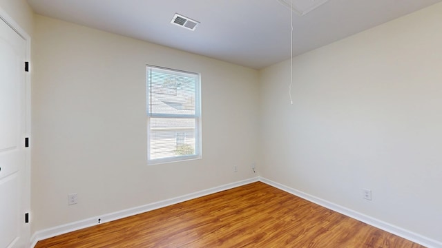 unfurnished room featuring light wood-type flooring, visible vents, baseboards, and attic access