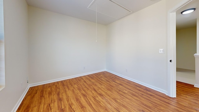 empty room with attic access, light wood-style floors, and baseboards