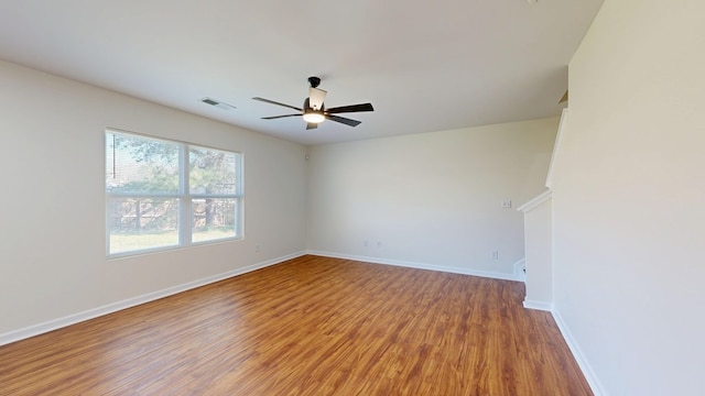 empty room with ceiling fan, visible vents, baseboards, and wood finished floors