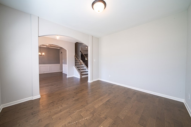 spare room featuring arched walkways, dark wood finished floors, baseboards, and stairs