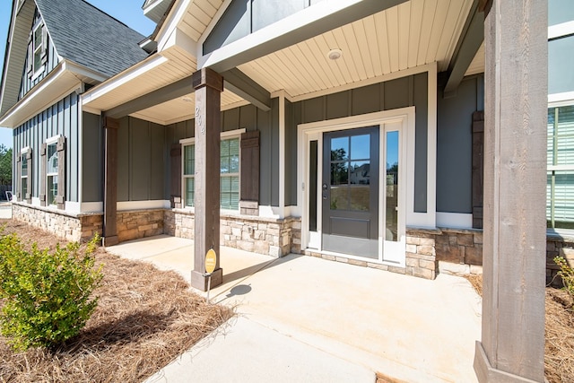 doorway to property featuring board and batten siding, stone siding, roof with shingles, and a porch