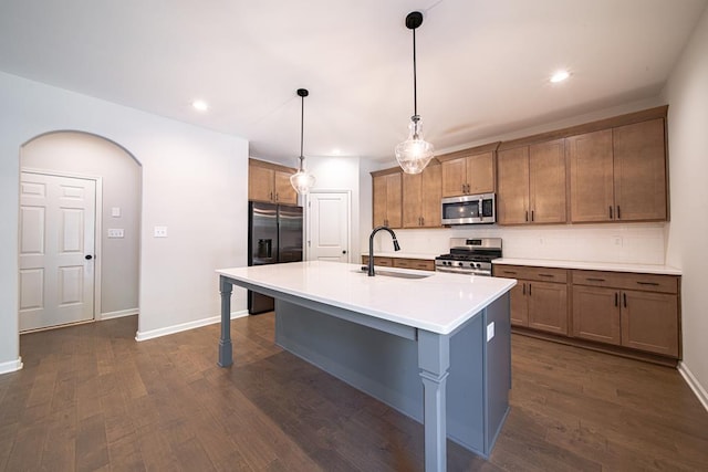 kitchen with arched walkways, dark wood-style flooring, a sink, appliances with stainless steel finishes, and an island with sink