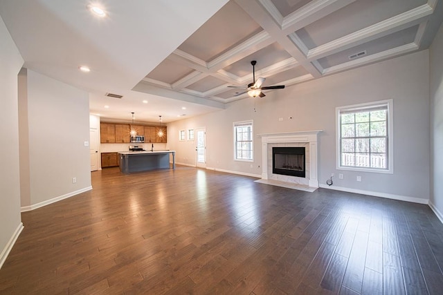 unfurnished living room with a tile fireplace, dark wood-style flooring, coffered ceiling, visible vents, and a wealth of natural light