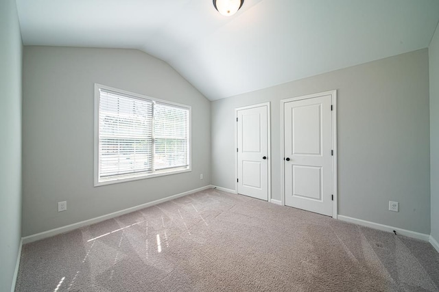 unfurnished bedroom with vaulted ceiling, carpet flooring, and baseboards