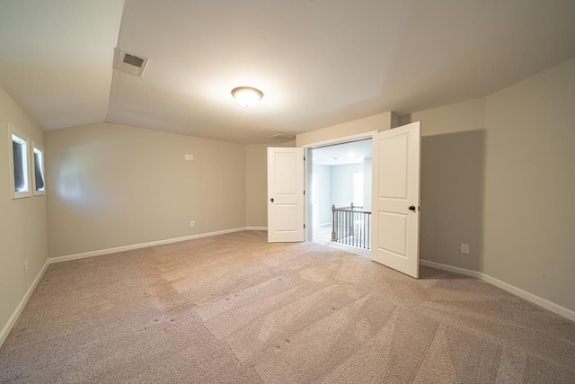 unfurnished room with light carpet, visible vents, baseboards, and lofted ceiling