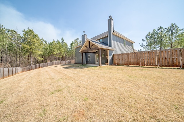 rear view of property with a fenced backyard, a yard, and a chimney