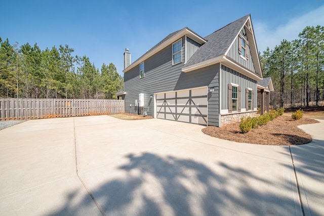 view of side of property featuring an attached garage, fence, concrete driveway, stone siding, and board and batten siding