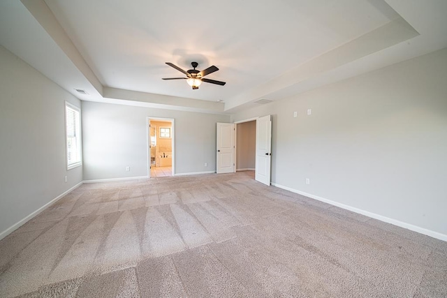 spare room with light carpet, a tray ceiling, and baseboards