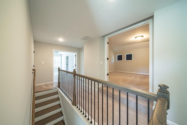 hallway with baseboards, visible vents, carpet flooring, and an upstairs landing