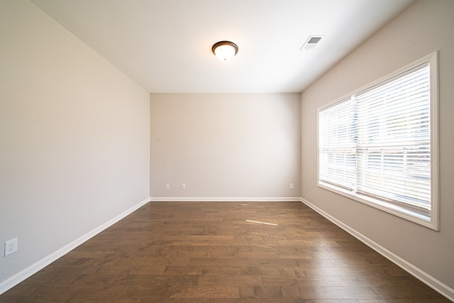 spare room featuring dark wood-style floors, visible vents, and baseboards