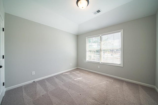 carpeted empty room featuring visible vents, vaulted ceiling, and baseboards