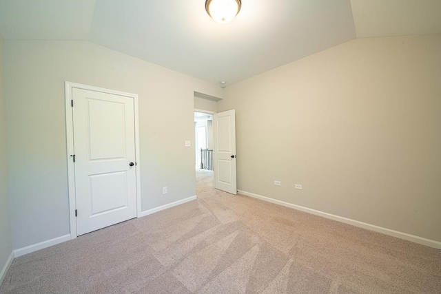 unfurnished bedroom with lofted ceiling, light carpet, and baseboards