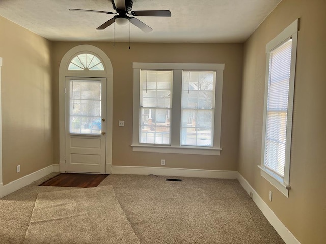 foyer entrance with ceiling fan and carpet flooring