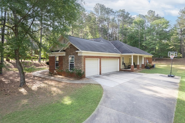 view of side of property with a porch, stone siding, driveway, a garage, and a lawn
