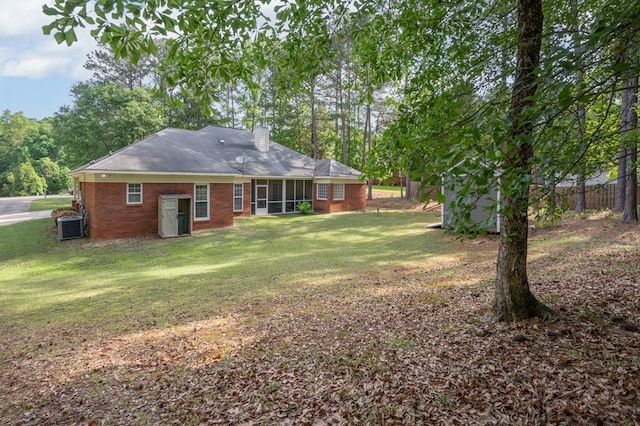back of house featuring a chimney, a lawn, brick siding, a sunroom, and central AC unit