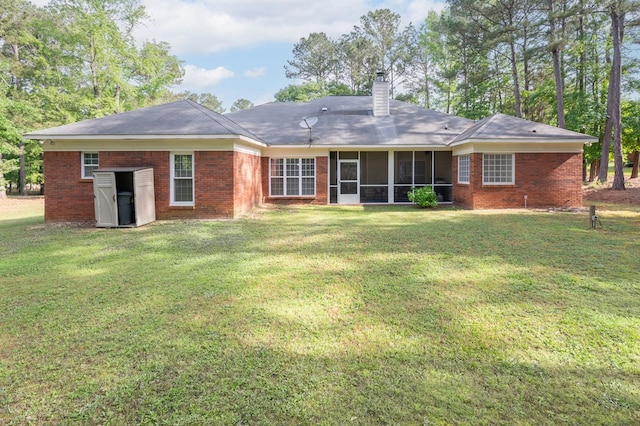 back of property featuring a chimney, a yard, brick siding, and a sunroom
