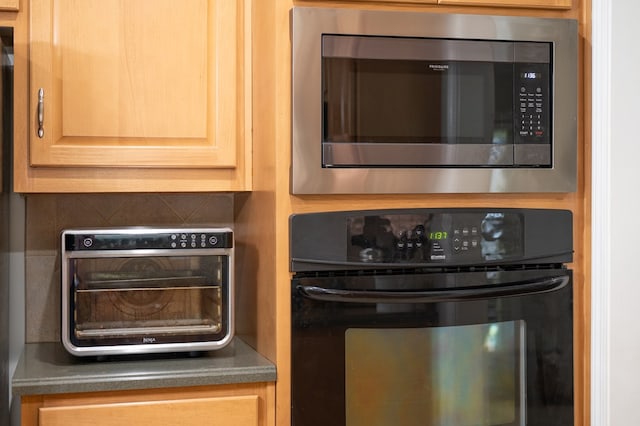 kitchen featuring stainless steel microwave, black oven, a toaster, light brown cabinetry, and dark countertops